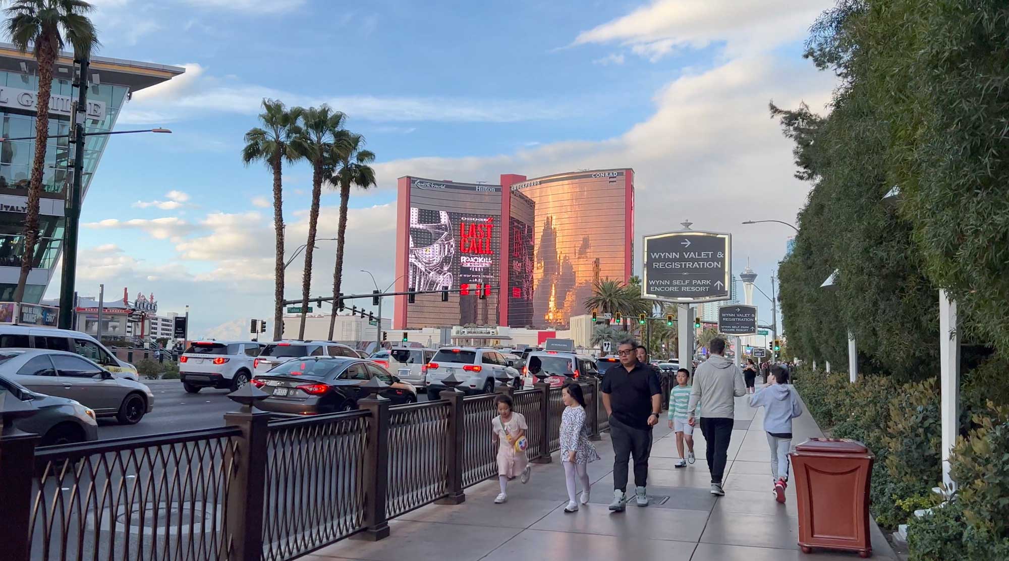 people waling on strip In front of last call billboard